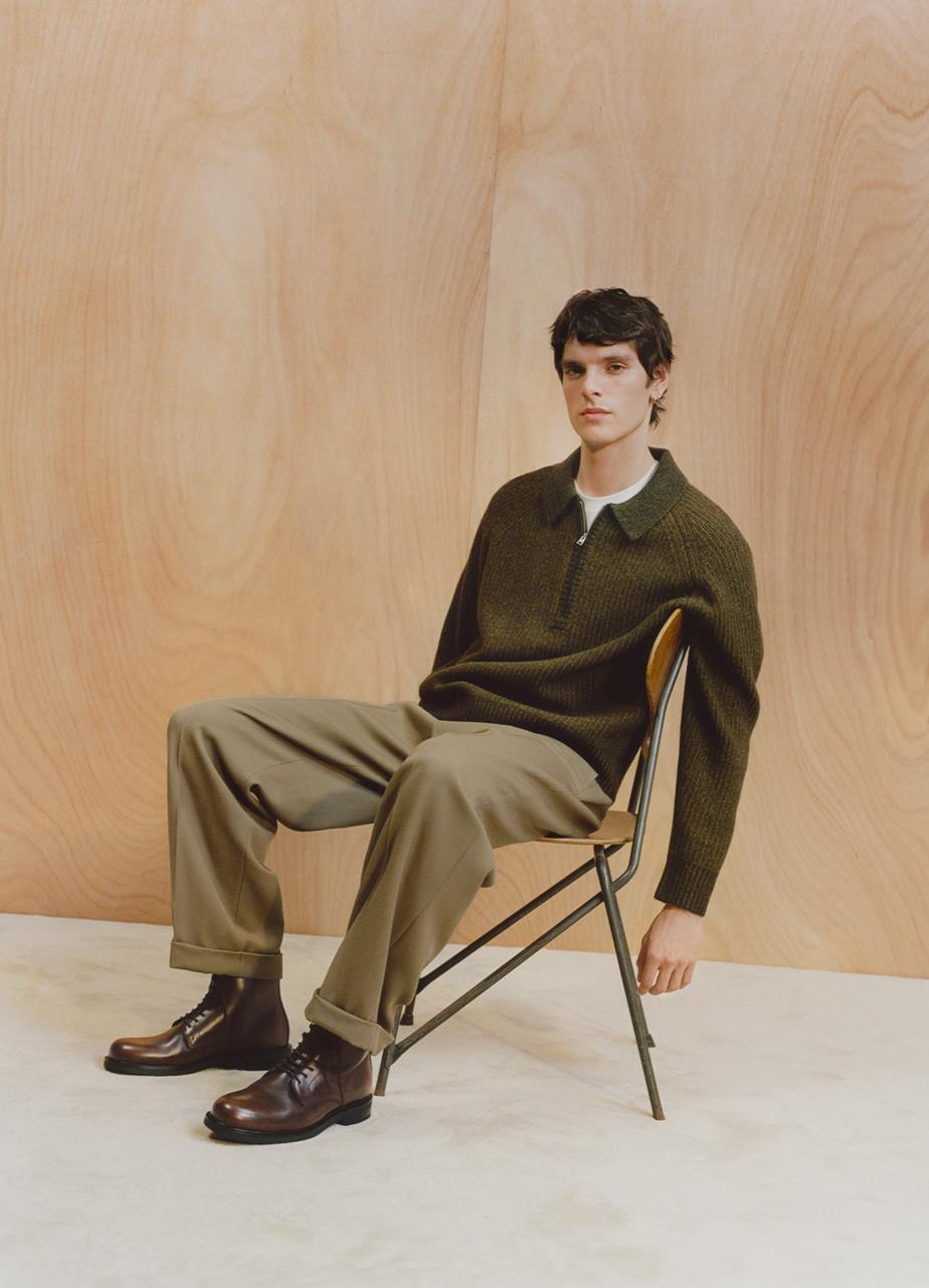A man in a chair poses against a white wall, highlithing a pair of brown lace-up Floyd boots