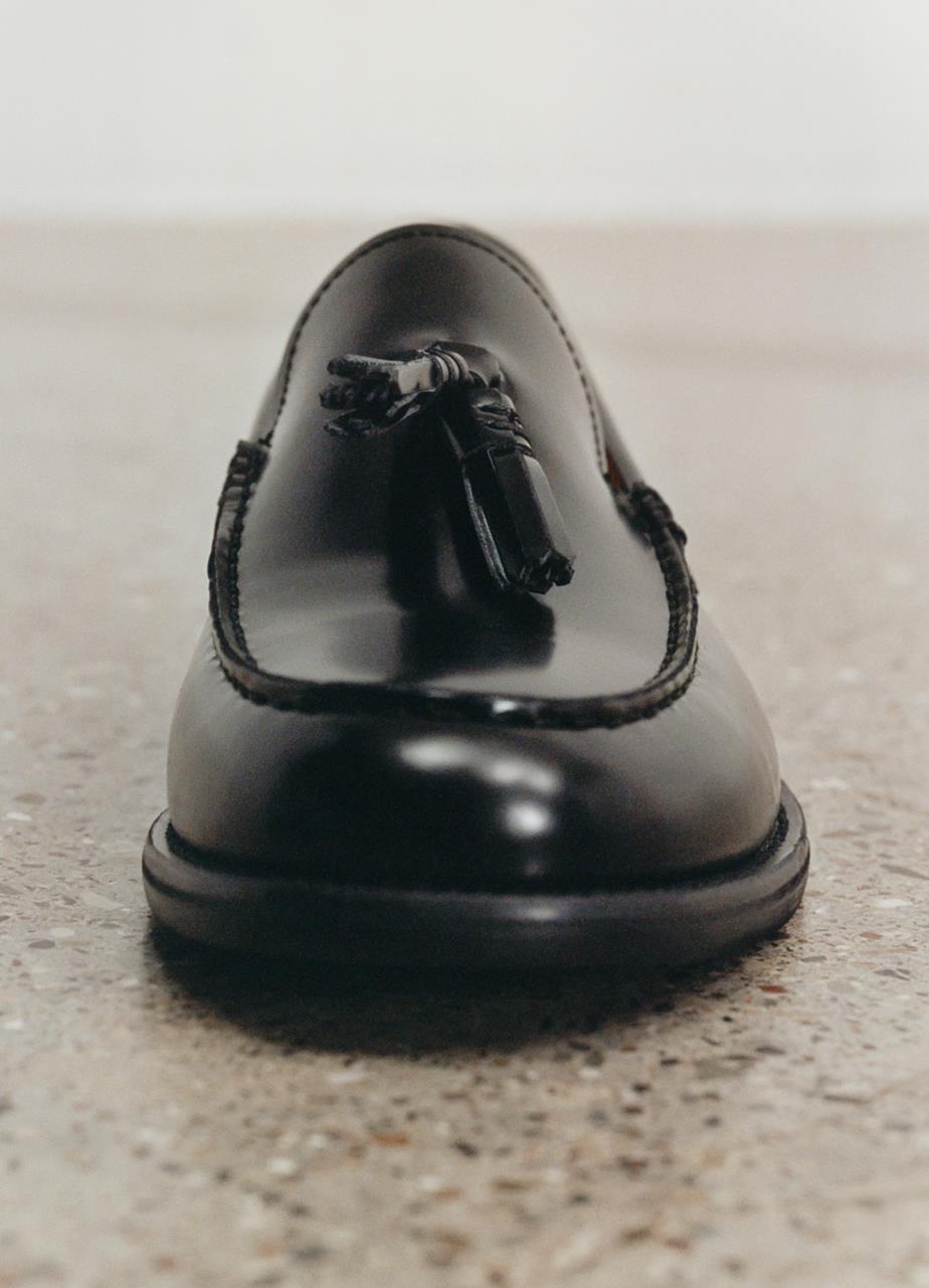 A close-up picture of the front of a black Steven Loafer with a tassel on top of the shoe