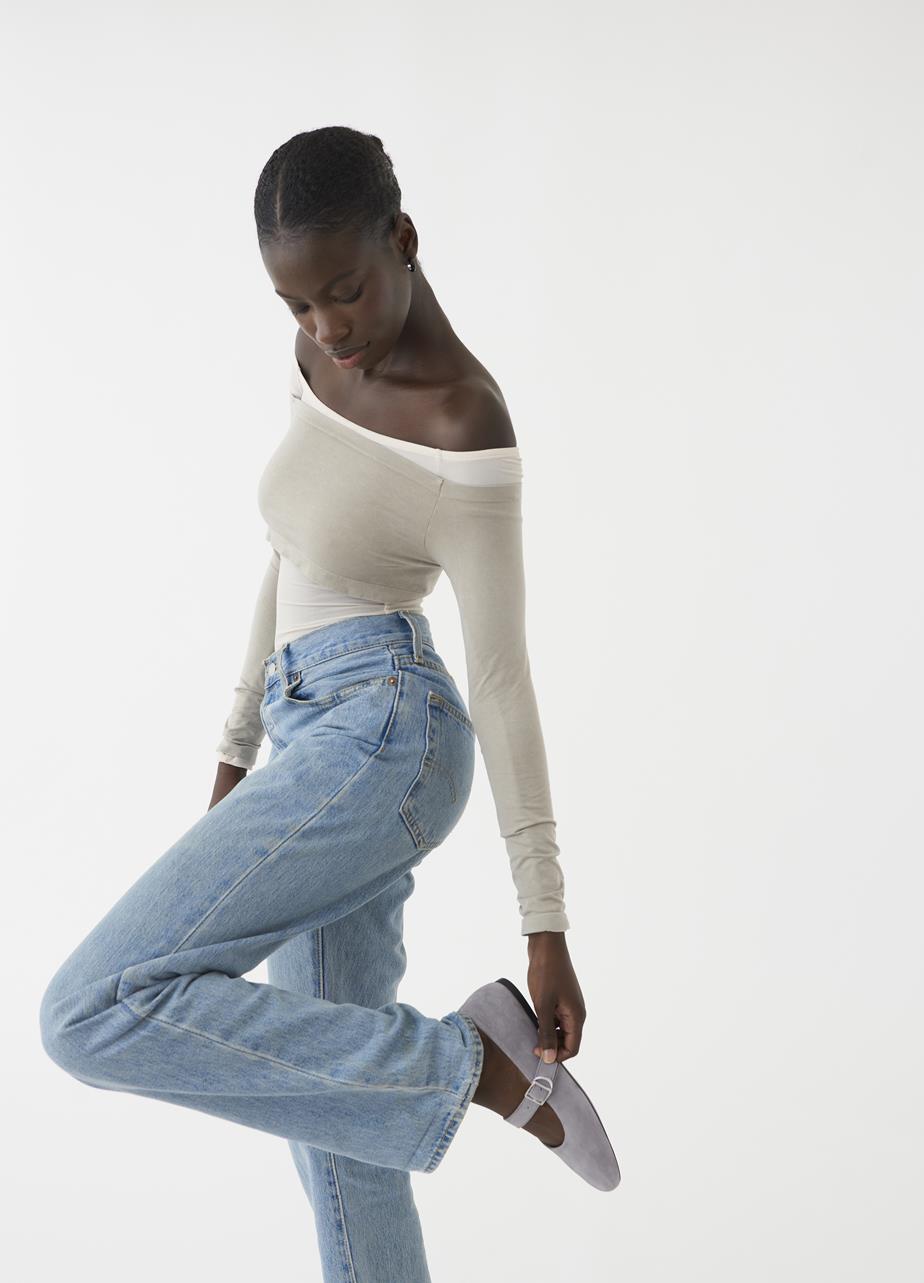 Female model wearing grey Mary Jane flats, paired with light blue jeans and a white off-shoulder top.