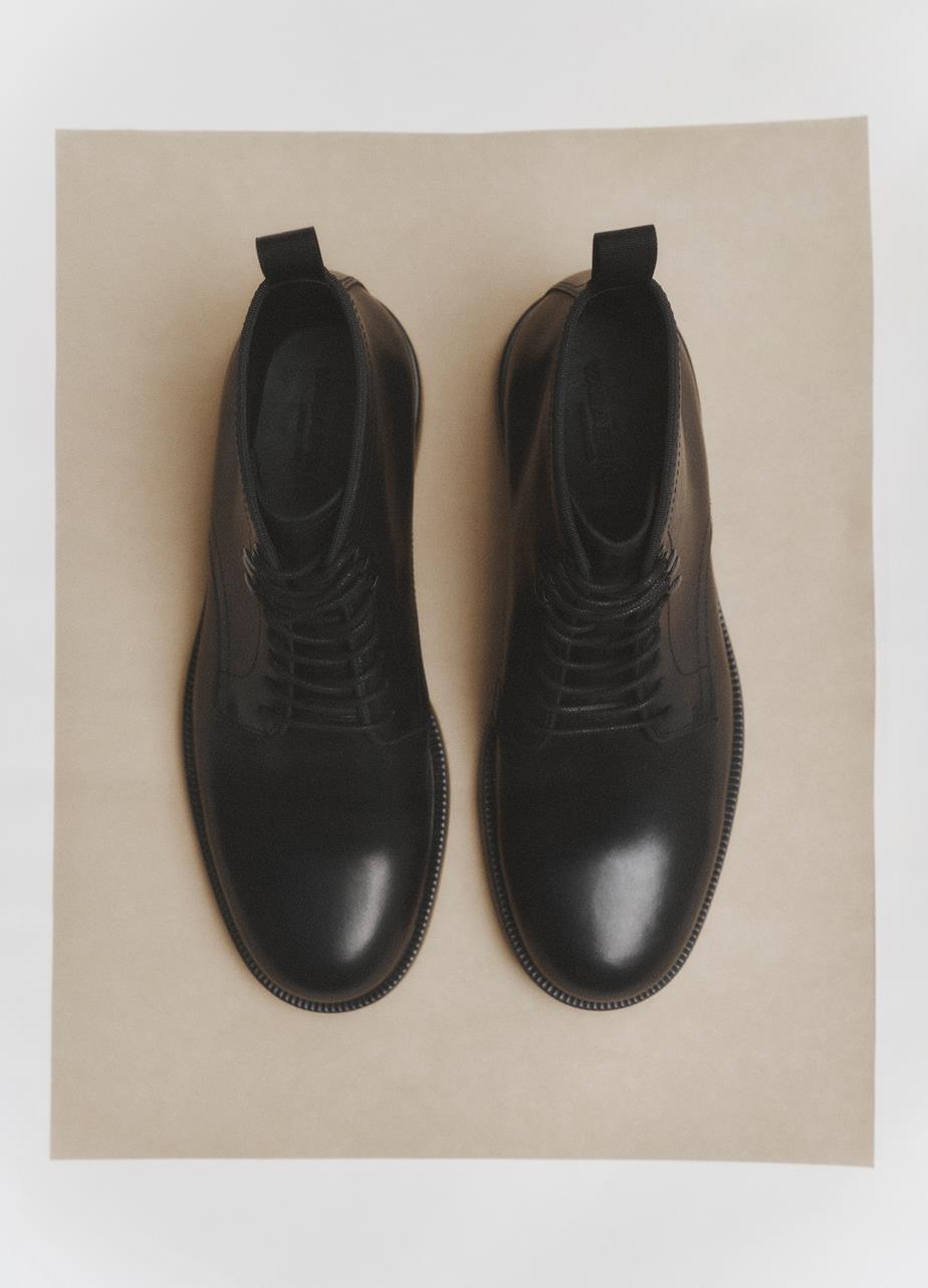 A pair of black leather lace-up Floyd boots diplayed from above on a piece of beige paper