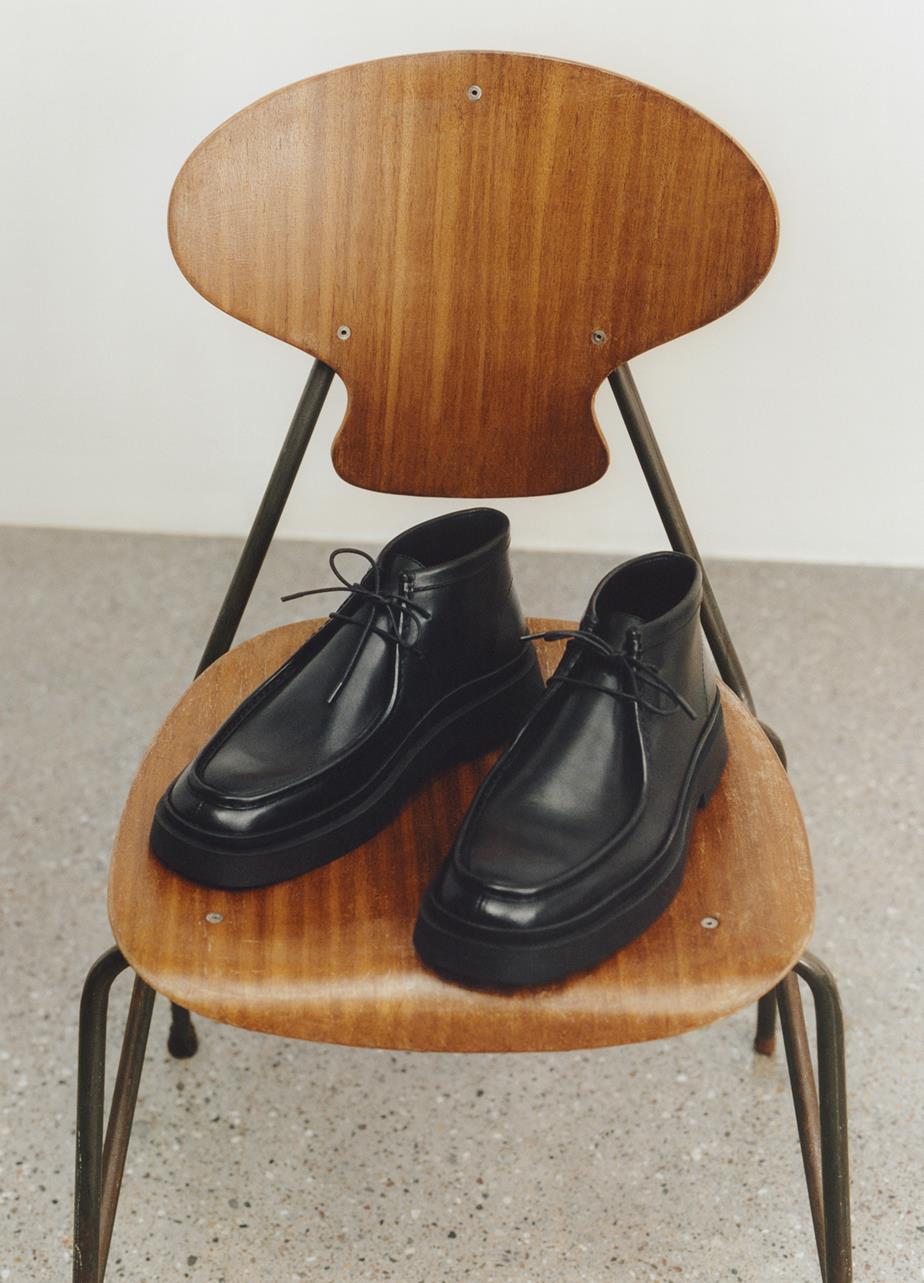 A pair of black leather Mike Boots displayed on a wooden chair