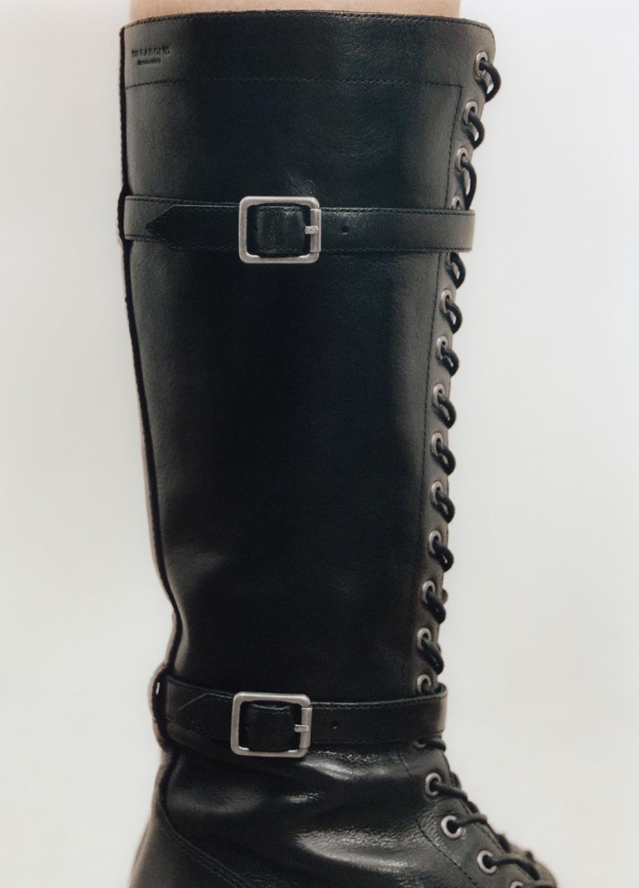 A close-up picture of the Karlie Tall Boot in black leather featuring buckels and metal accents