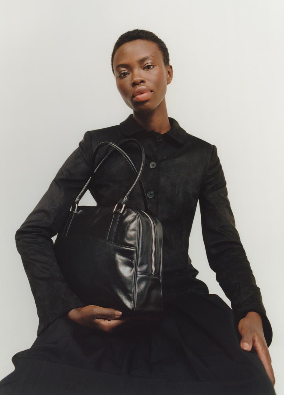A woman sitting with the black leather Nomi Bag under her arm