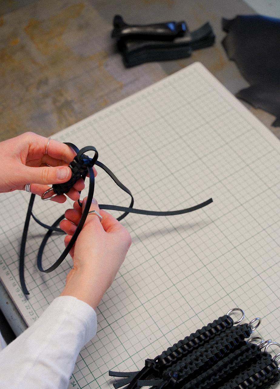 Hands braiding leather strings, making a bag charm in the studio.