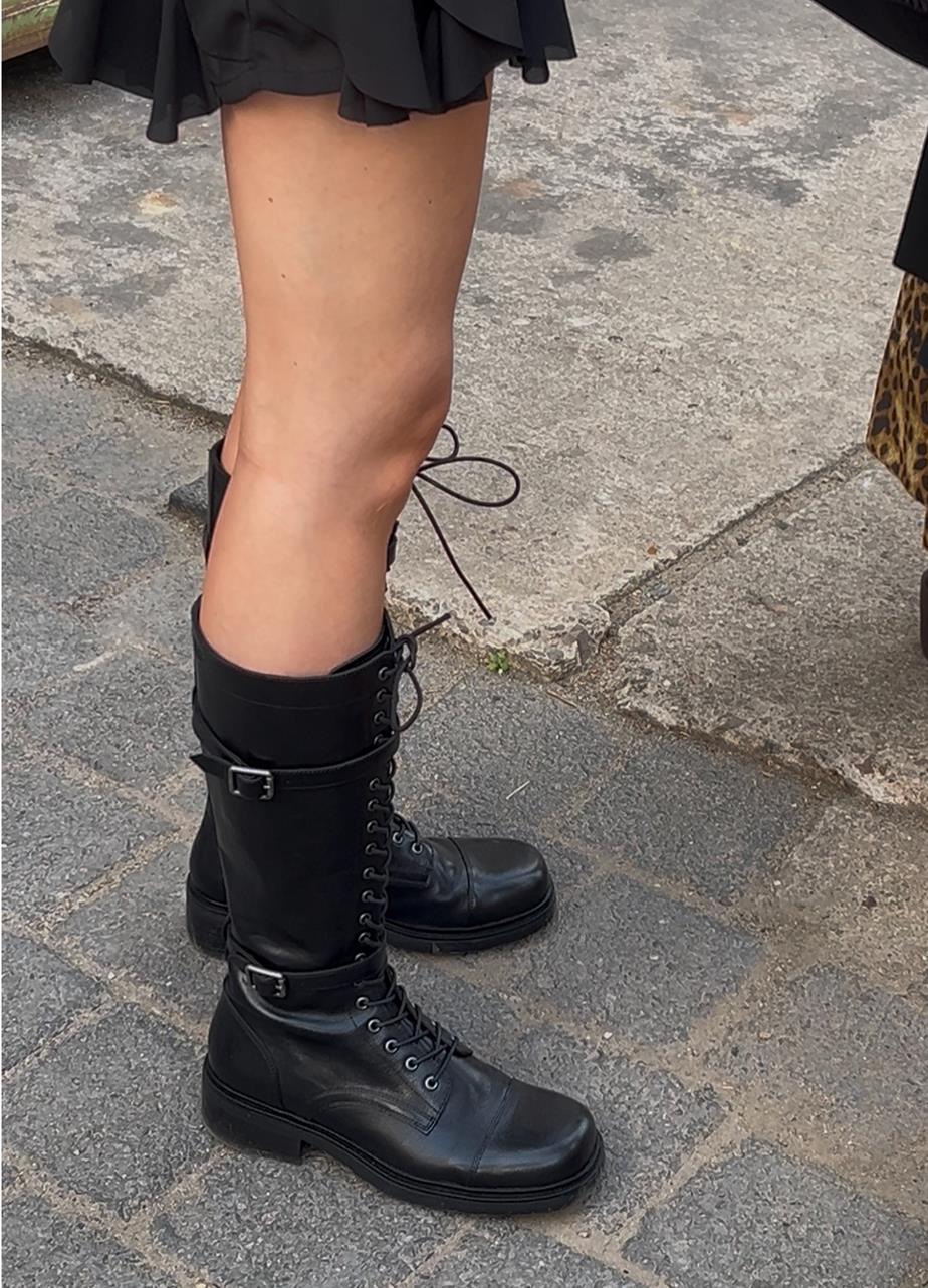 A person in a short skirt and the tall Karlie boots standing outside on the cobblestone