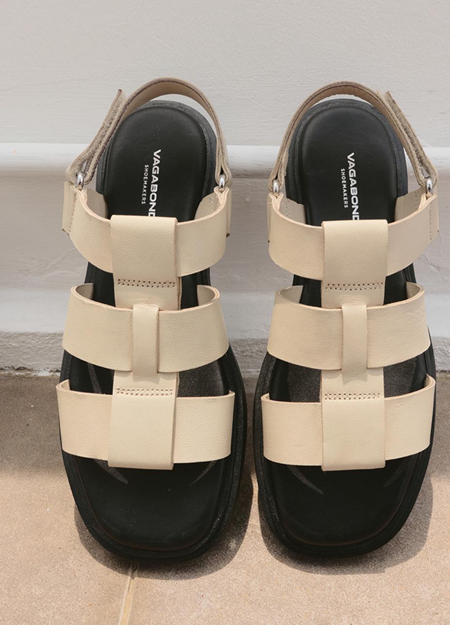 A pair of sandals featuring straps, leaning against a wall.