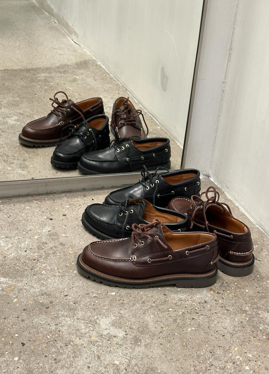 Brown and black boat shoes placed by a mirror on a concrete floor.