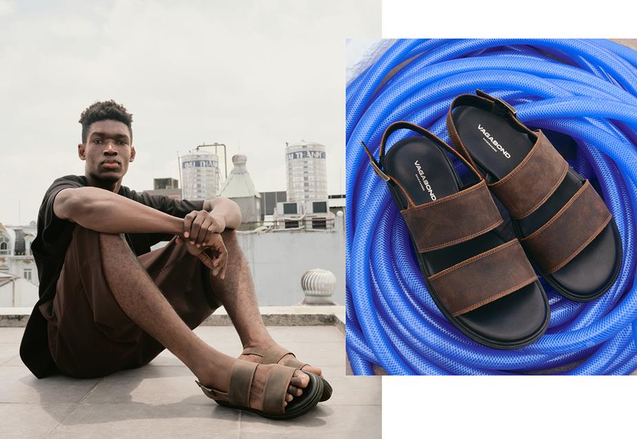 A man sitting on the ground beside a pair of sandals, in a casual outdoor setting.