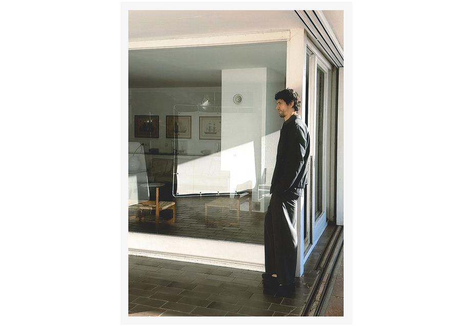 A man leaning against a house wall in the sunlight