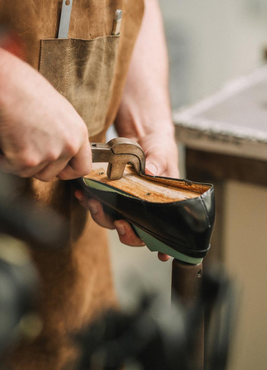 Shoemaker in an apron working by hand on a leather shoe using shoemaking tools